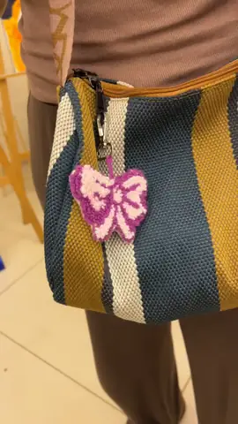 Pink bow punch needle charm clipped to a bag